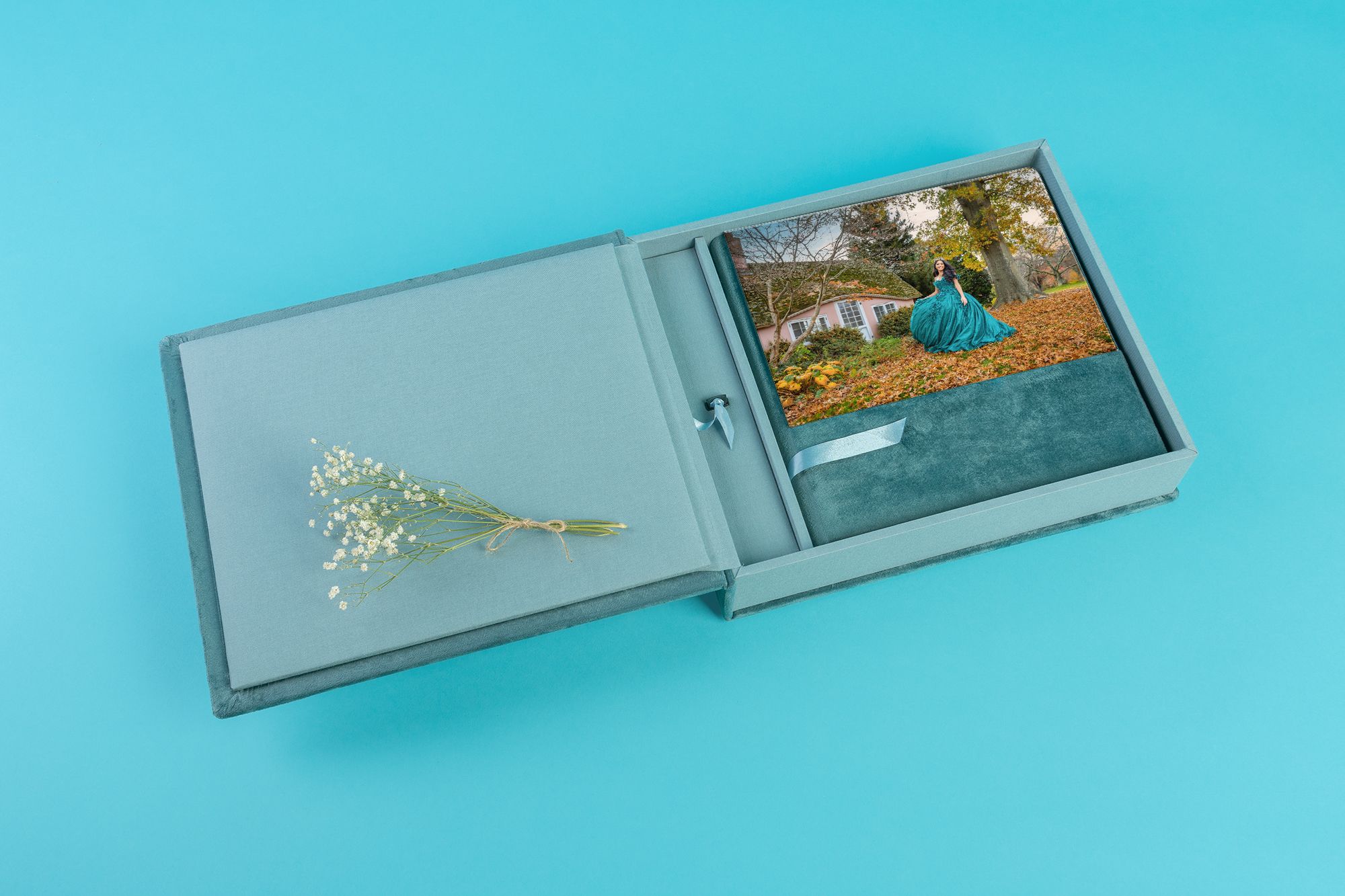 Gray photo album with dried flowers and prints on turquoise background.