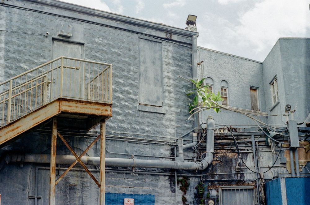 Industrial building exterior with metal staircase and grey walls featuring exposed utilities and architectural details.