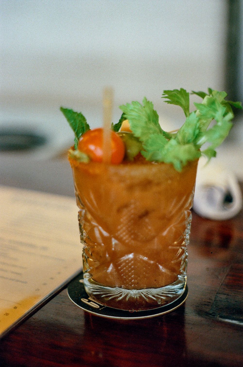 A Bloody Mary cocktail garnished with celery and cherry tomato served in an ornate cut crystal glass.