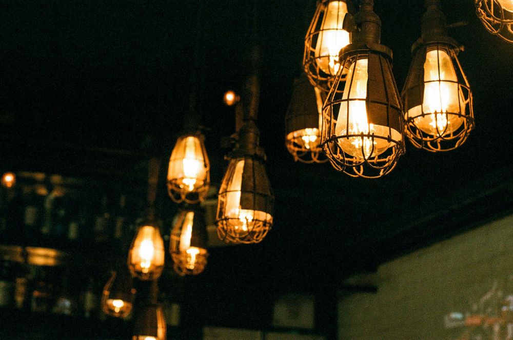 Vintage industrial pendant lights with metal cages glow warmly against a dark background in a dimly lit space.