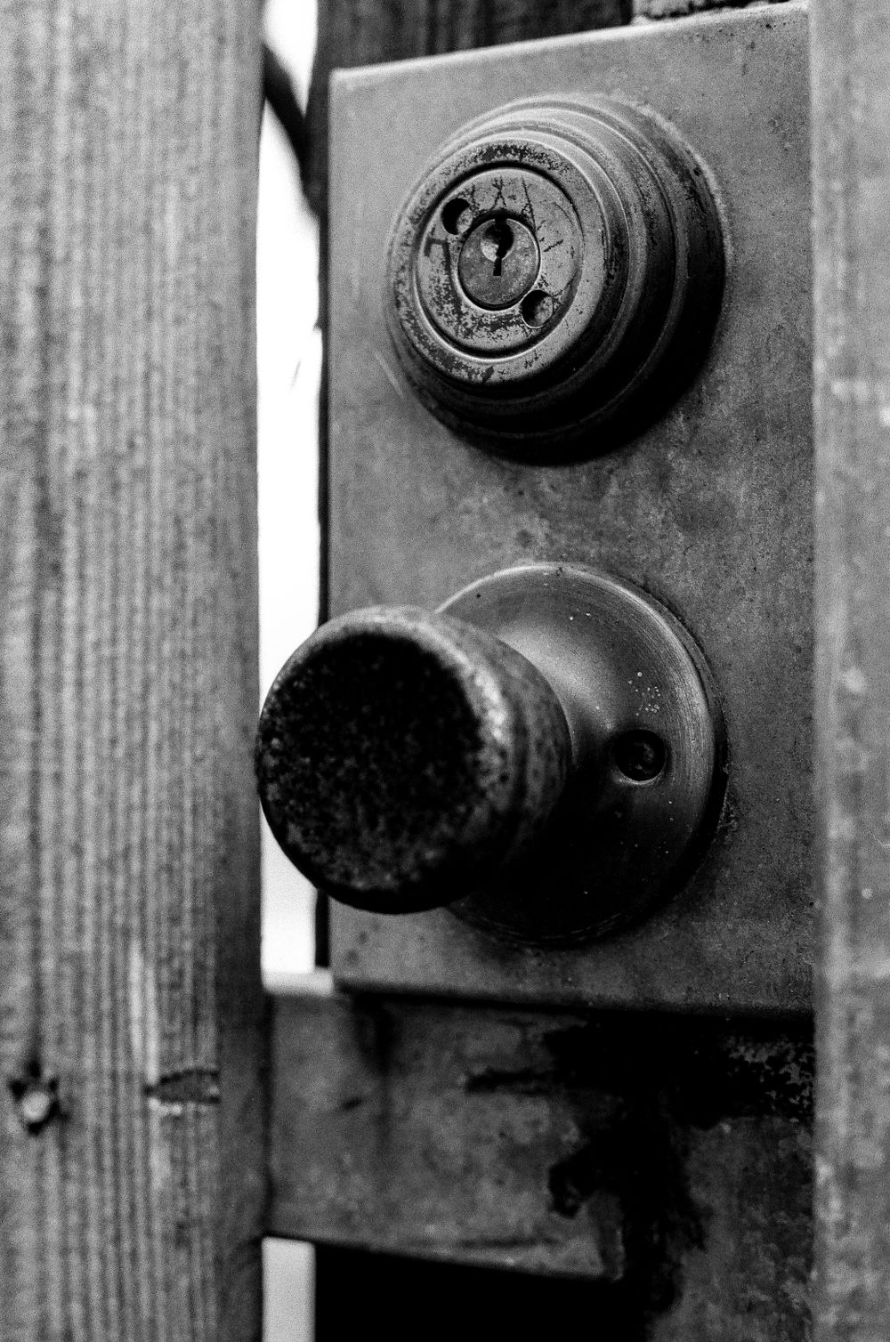 A vintage black and white photo shows a weathered doorknob and lock mechanism on a wooden door.