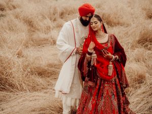 A couple in traditional Indian wedding attire pose intimately in a dreamy field with dried grass and desert tones.