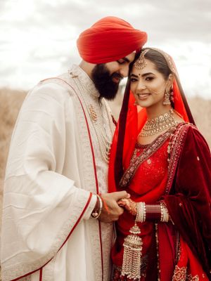A tender Sikh wedding portrait shows a couple in traditional attire with the bride in red and groom in cream colored clothing.