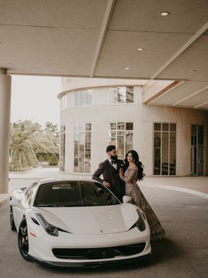 A couple poses with a white Ferrari 458 Italia under a modern building entrance.
