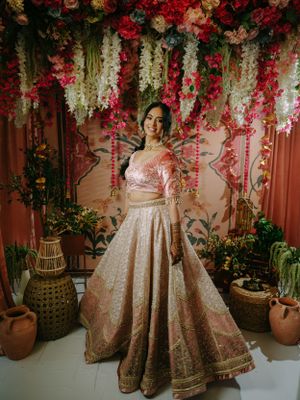 Traditional bridal attire featuring a blush pink lehenga against a stunning floral backdrop with hanging blooms and clay pots.