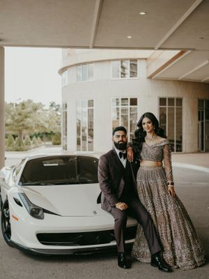 A couple in formal attire poses beside a white luxury sports car outside a modern building.