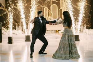 A couple dances together during their wedding celebration with sparklers and elegant lighting in the background.