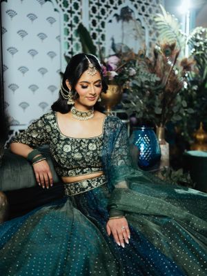 A traditional Indian lehenga in teal and black with intricate embroidery and jewelry, photographed with a blue lantern and decor.