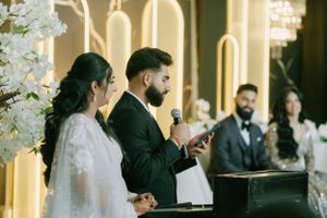 A couple participates in their wedding ceremony in front of illuminated arches and floral decorations.