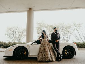 A glamorous couple poses next to a white luxury sports car, with the woman wearing a sparkly gold ballgown.