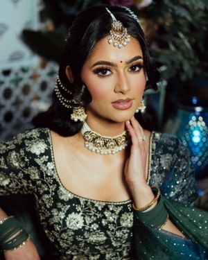 Person wearing traditional South Asian bridal attire with ornate jewelry and emerald green dress in elegant portrait.