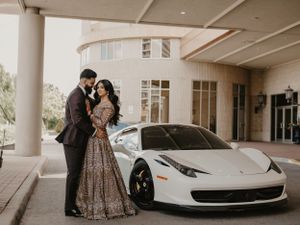 A white Ferrari 458 Italia parked under building columns with a romantic couple in formal attire standing beside it.