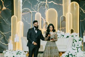 A couple stands in front of a luxurious gold and white backdrop with illuminated arches.