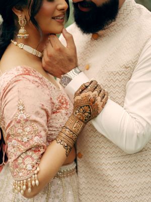 Elegant intricate henna designs adorn the bride's hand as couple shares an intimate moment.