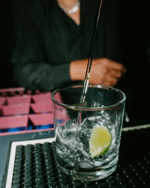A cocktail being stirred in a rocks glass with ice and a lemon garnish.