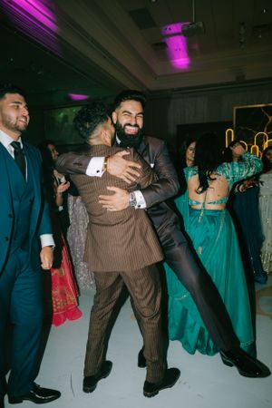 Wedding reception dance floor with celebratory hugs and guests in formal attire under purple lighting.