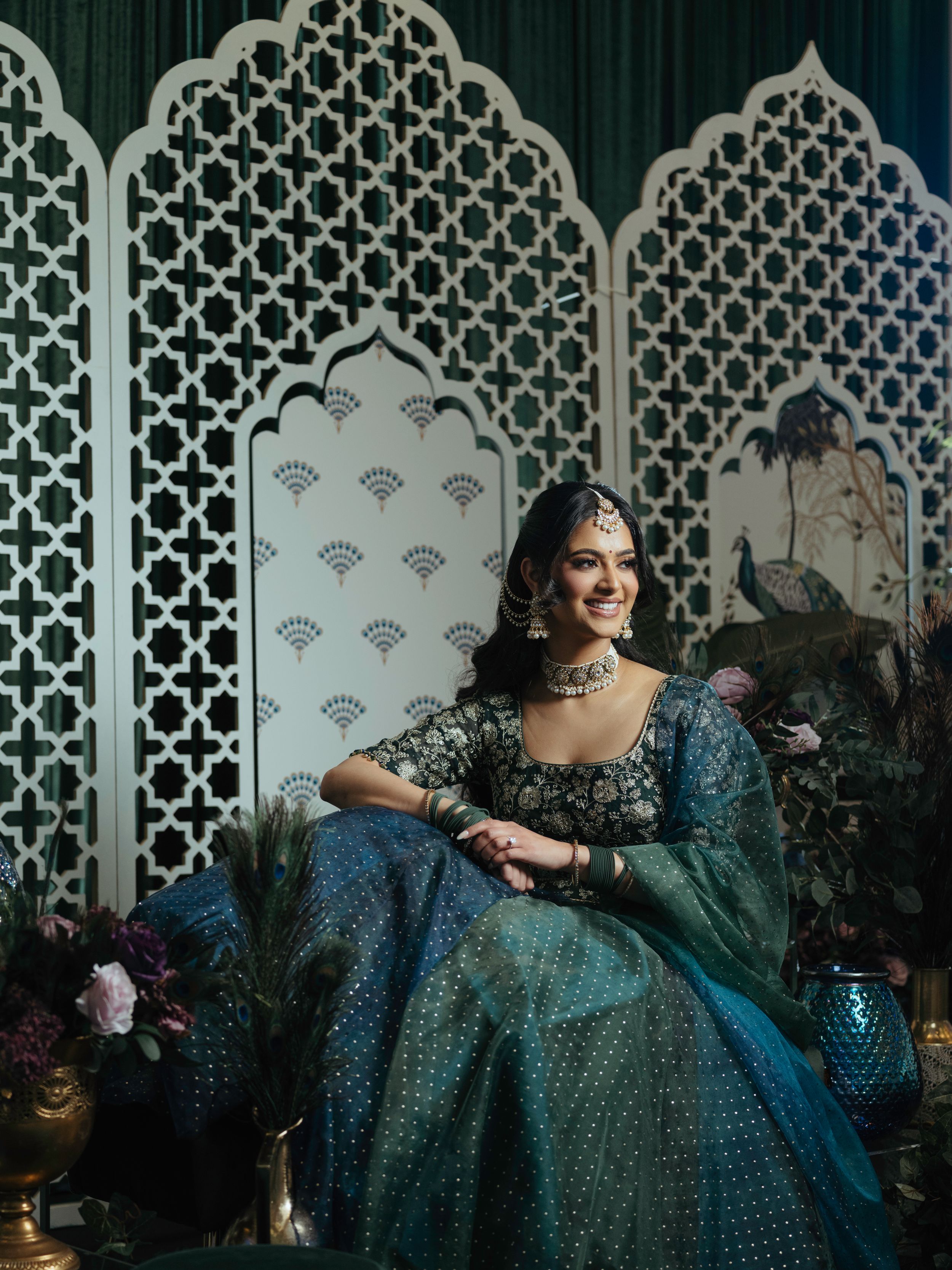 Ornate turquoise and silver lehenga set against decorative white latticed backdrop with floral arrangements.
