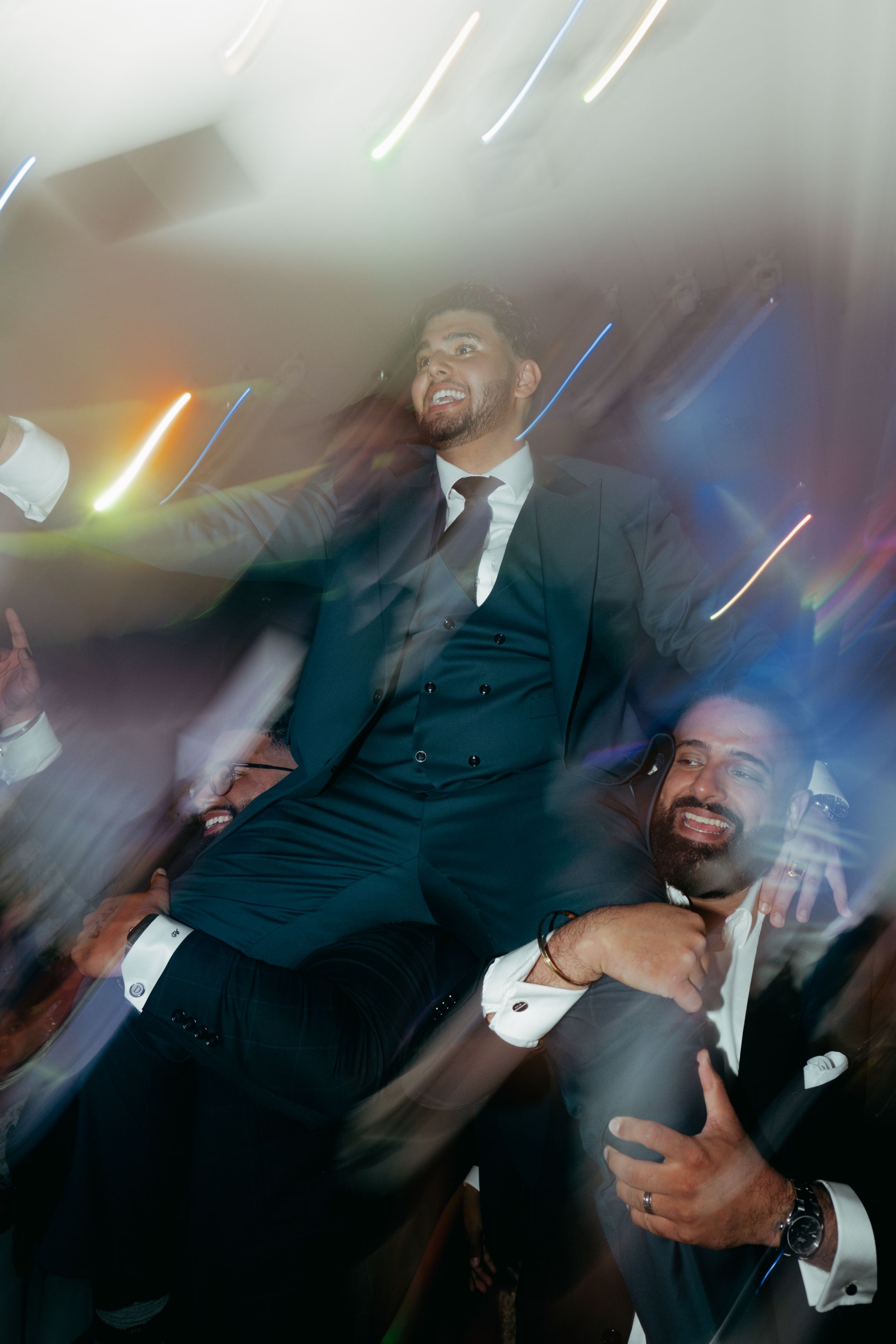 Men in suits celebrate at a party with motion blur and colorful lighting effects.