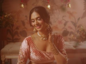 Soft lighting illuminates a person wearing a pink embroidered lehenga with delicate jewelry in a dreamy setting.