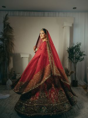 Traditional South Asian bridal attire in deep red lehenga with intricate gold embroidery and matching long veil.