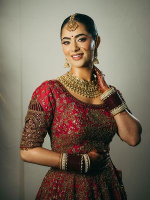 Traditional Indian bridal attire featuring a red and gold embellished lehenga with ornate jewelry and styling.