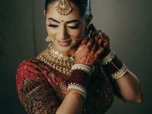 Traditional Indian bride in red lehenga with ornate gold jewelry and mehndi adorned hands poses during wedding ceremony.