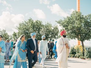 A group of people walking outdoors wearing traditional Indian and Sikh attire during a sunny day celebration.