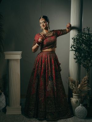 Traditional Indian bridal attire featuring an elegant red and gold embroidered lehenga in a classic studio setting.