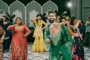Joyful guests dancing and celebrating at an Indian wedding reception with decorative lattice backdrop.