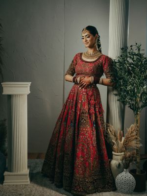 Elegant red and gold embroidered lehenga photographed against a classical interior with decorative elements.