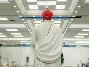 A person wearing a white garment and red cap stands facing away from the camera in a bright indoor space.