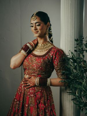 Traditional South Asian bridal attire featuring an embellished red lehenga with intricate gold details and statement jewelry.