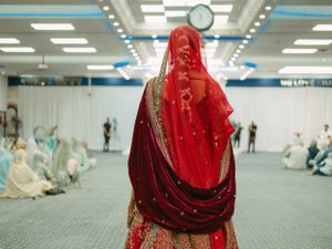 Bride in vibrant red traditional attire with gold embellishments during a wedding ceremony.