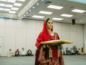 Traditional Indian wedding ceremony with bride carrying ceremonial plate in decorated hall.