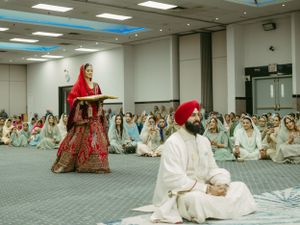 Traditional Sikh wedding ceremony taking place in a large carpeted room with guests seated on the floor.
