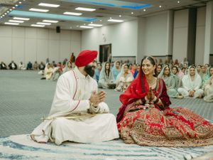 Traditional Sikh wedding ceremony taking place in a large hall with guests seated on the floor.