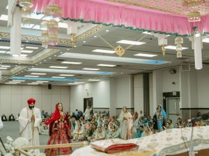 Wide view of a Sikh wedding ceremony in a decorated banquet hall with pink drapery and guests.