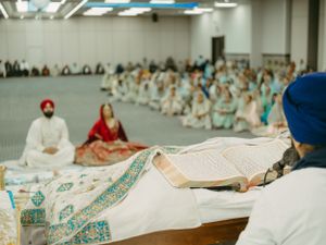 People gather in a Sikh temple for a traditional religious service with white-clad worshippers sitting on the floor.