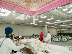 View of a Sikh wedding ceremony in a large hall with guests seated on the floor.