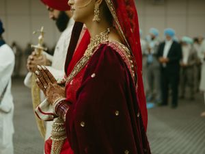 A traditional Indian wedding scene showing detailed embroidery of a deep red bridal outfit with gold accents.
