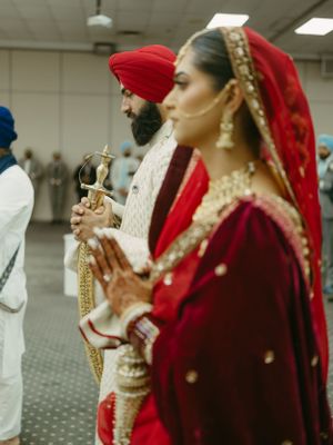 Traditional Sikh wedding ceremony showing participants in red and white attire during prayer.
