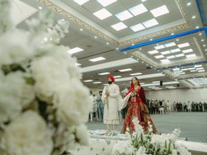 Elegant wedding ceremony setup with white floral decorations and participants in traditional red attire.