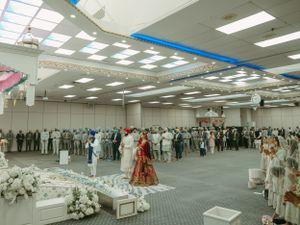 Wide view of a Sikh wedding ceremony hall with guests gathered around and white floral decorations.