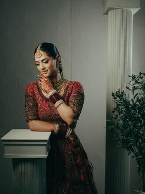 A stunning portrait in traditional South Asian wedding attire with intricate jewelry and red embroidered dress.
