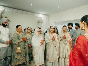 A group in traditional Indian attire celebrates together at an indoor gathering wearing light colored and red outfits.