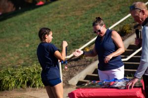 People in navy blue clothing chat during an outdoor event by a table on a sunny day.