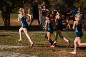 Cross country runners in navy uniforms compete during an autumn race on a grassy course.
