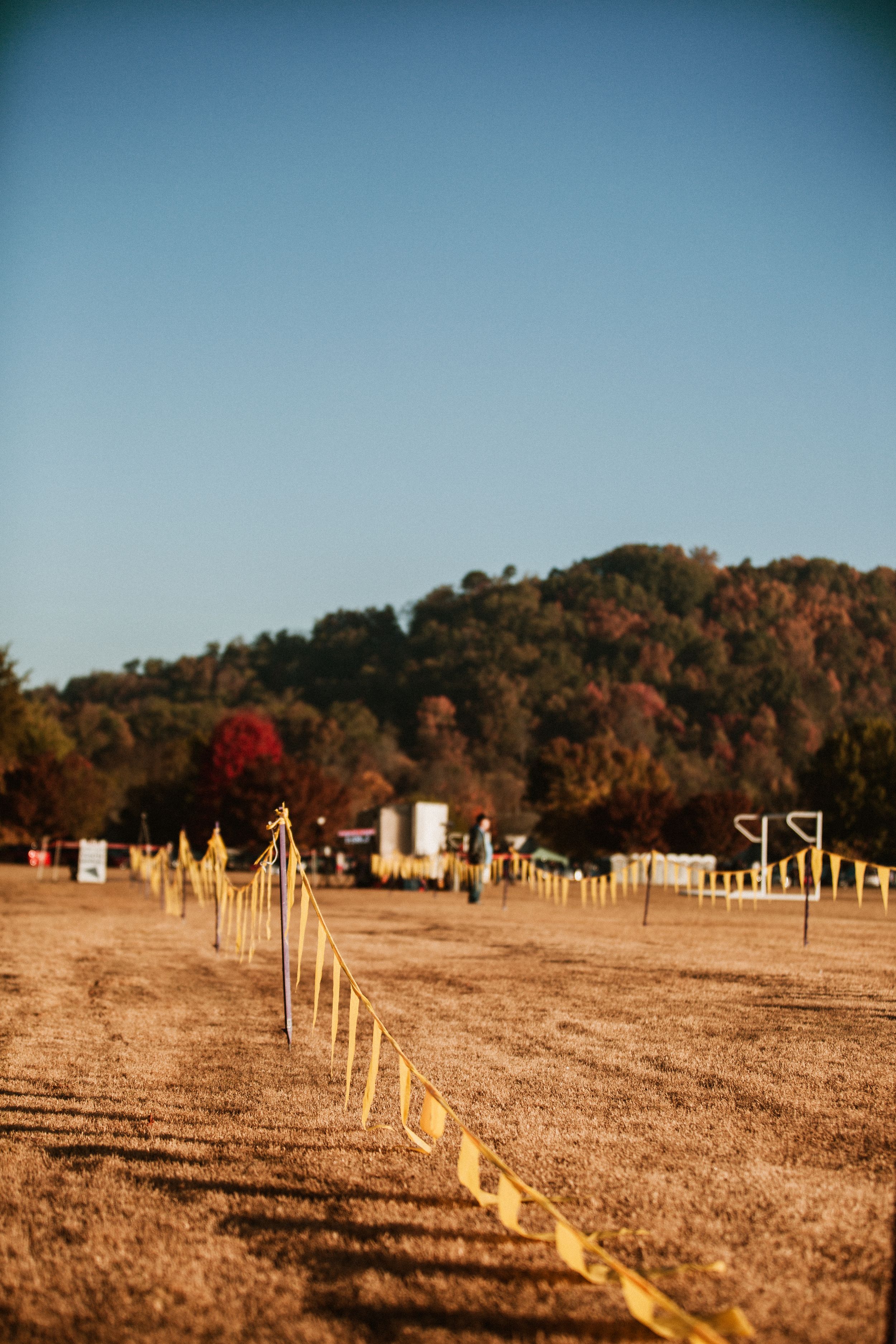 Yellow ropes mark a pathway across a dusty field with autumn trees on rolling hills in the background.