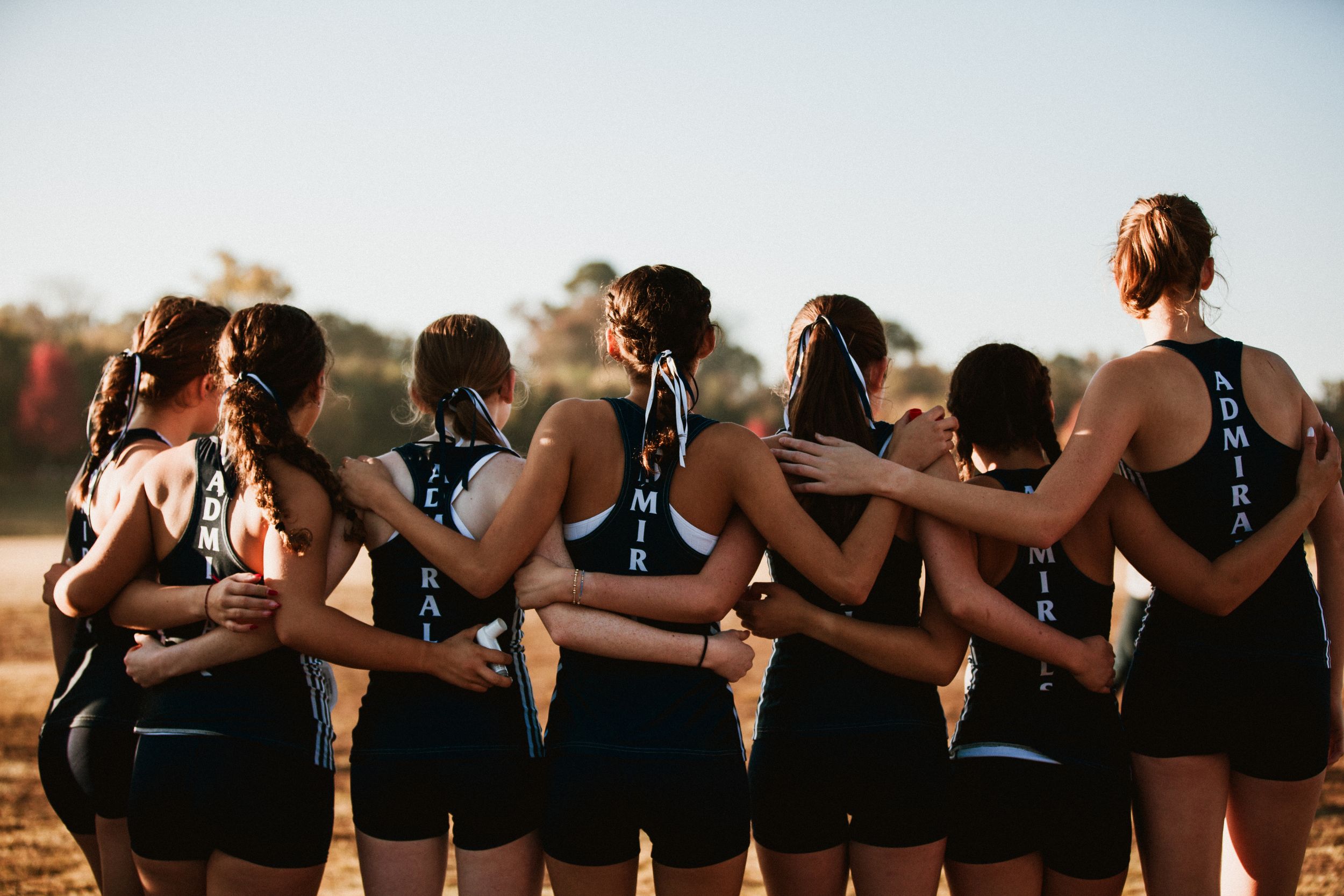 Team of runners in matching uniforms embrace together in a supportive huddle at sunset.