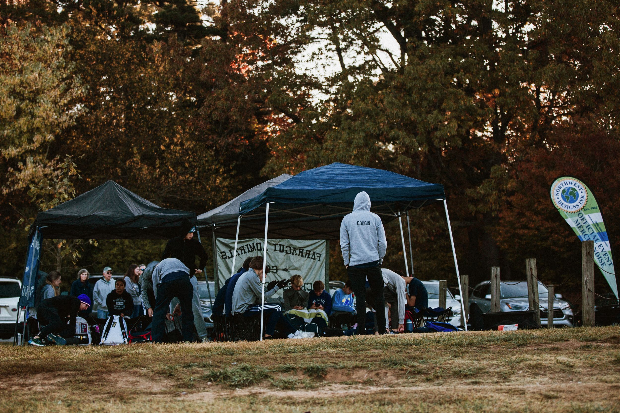 Outdoor community gathering with pop-up tents and vendor booths set up in a park during sunset.